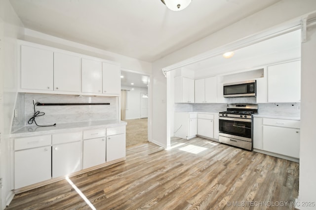 kitchen with white cabinets, backsplash, stainless steel appliances, and light hardwood / wood-style flooring