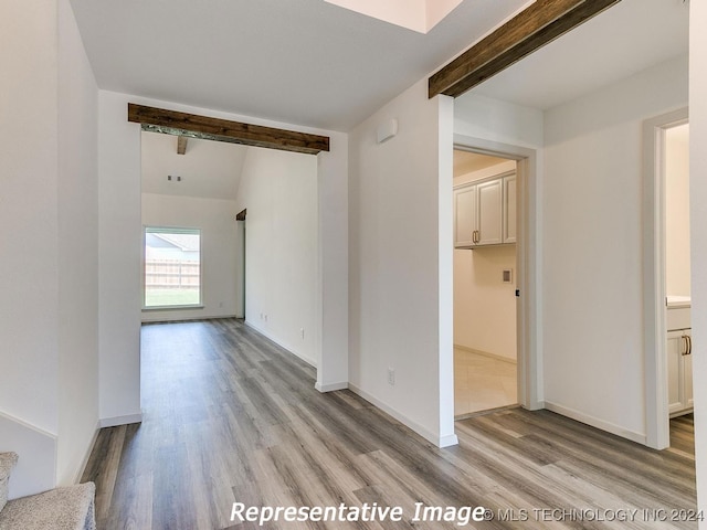 empty room featuring lofted ceiling with beams and light hardwood / wood-style floors