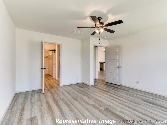 unfurnished bedroom with light wood-type flooring, a spacious closet, ceiling fan, and a closet