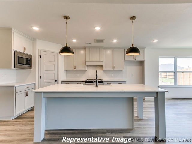 kitchen featuring an island with sink, stainless steel appliances, and decorative light fixtures