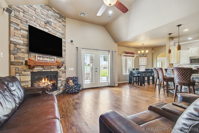 living room featuring french doors, a stone fireplace, high vaulted ceiling, dark hardwood / wood-style floors, and ceiling fan with notable chandelier