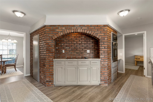 interior space with white cabinets, hanging light fixtures, appliances with stainless steel finishes, an inviting chandelier, and light wood-type flooring