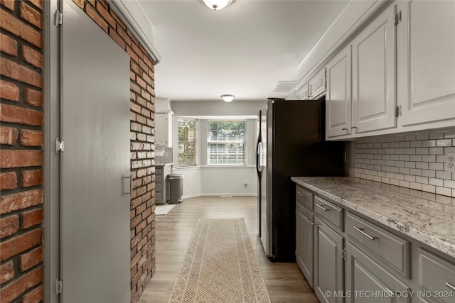 kitchen with gray cabinetry, light hardwood / wood-style floors, stainless steel fridge, light stone counters, and backsplash