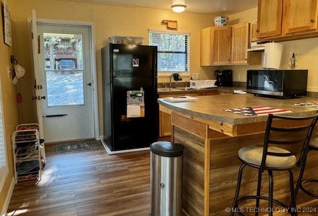 kitchen featuring stainless steel microwave, dark countertops, dark wood finished floors, freestanding refrigerator, and a breakfast bar area