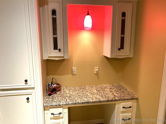 interior space with pendant lighting, white cabinetry, light stone counters, and built in desk