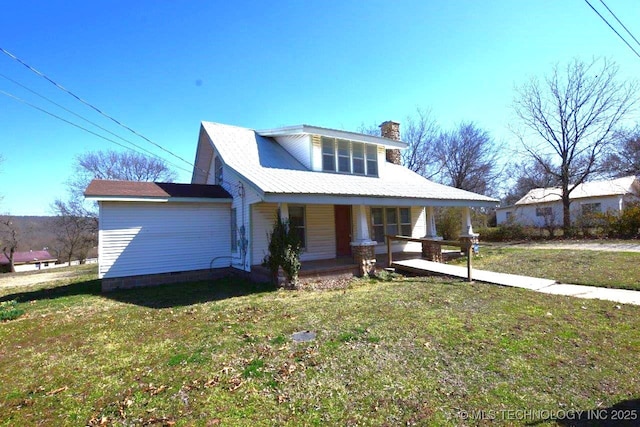 view of front of home with covered porch, a chimney, and a front yard