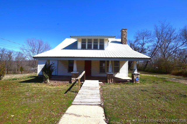 view of front of home with a porch, a front yard, metal roof, and a chimney