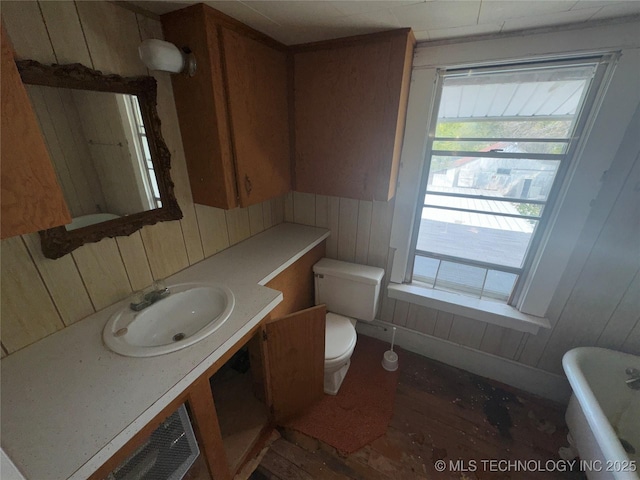 bathroom featuring a freestanding tub, toilet, wood walls, wood finished floors, and vanity