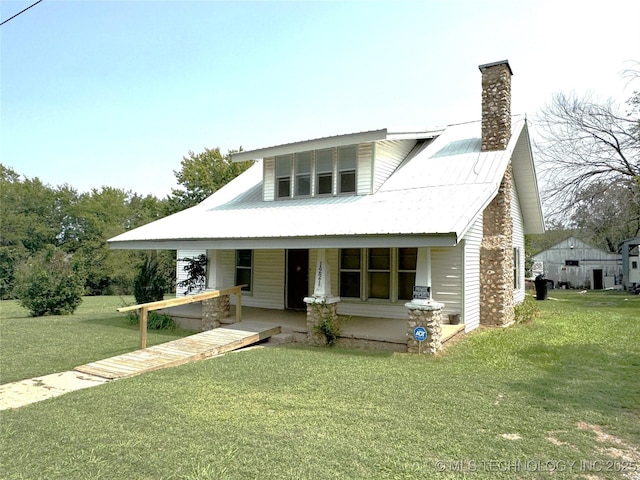 view of front of property featuring metal roof, a chimney, a front lawn, and a porch