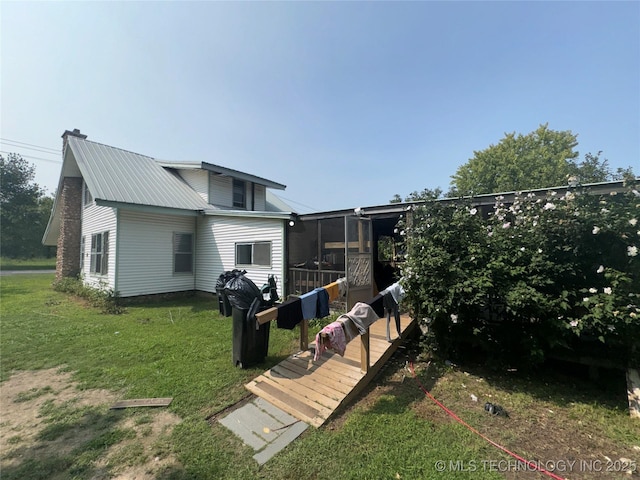 back of property featuring a sunroom, a chimney, metal roof, and a yard