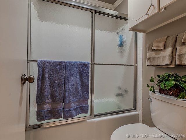 bathroom featuring toilet, ornamental molding, and bath / shower combo with glass door