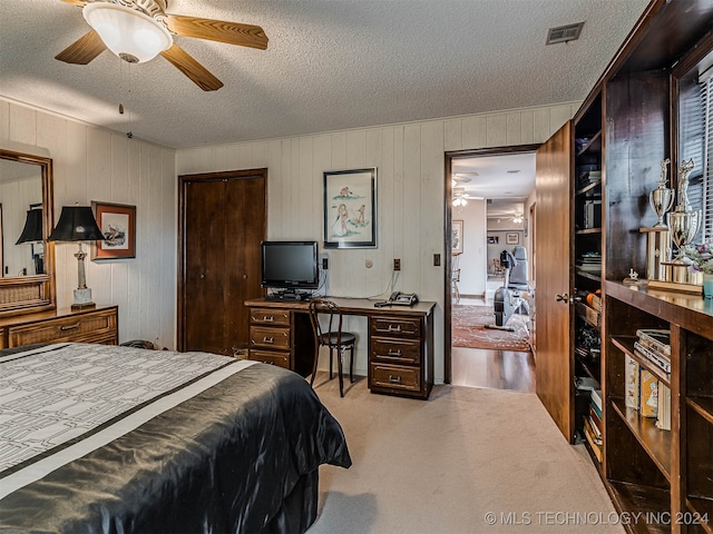 bedroom featuring ceiling fan, wooden walls, light carpet, and a textured ceiling