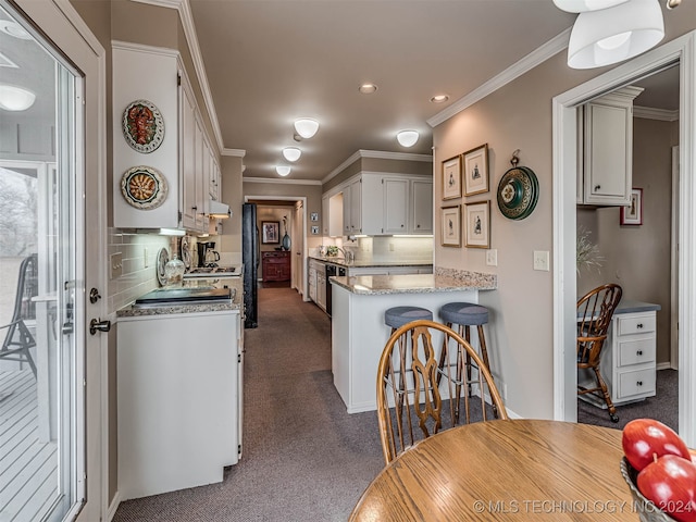 kitchen with ornamental molding, backsplash, kitchen peninsula, dark colored carpet, and white cabinets