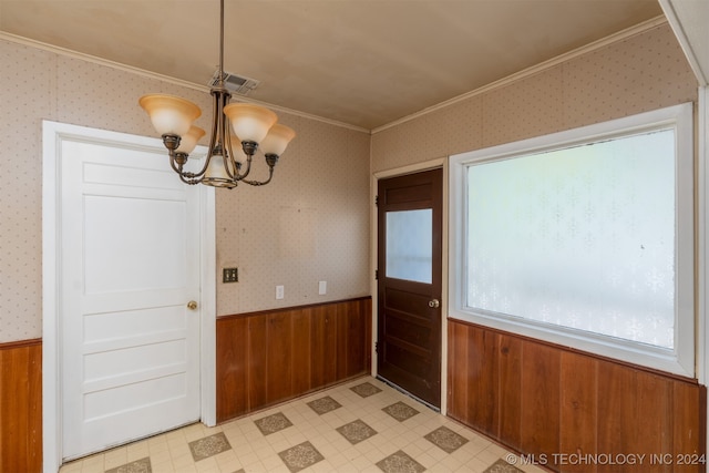 unfurnished dining area with ornamental molding, a chandelier, and wood walls