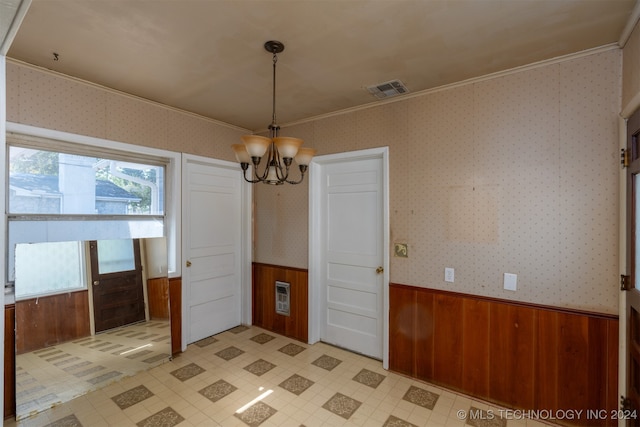 unfurnished dining area with crown molding, a chandelier, and wooden walls