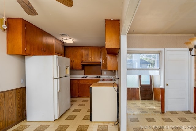 kitchen featuring ceiling fan, wood walls, stainless steel gas cooktop, sink, and white refrigerator