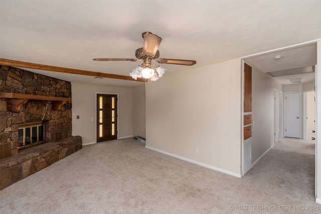 unfurnished living room with ceiling fan, a stone fireplace, and light colored carpet