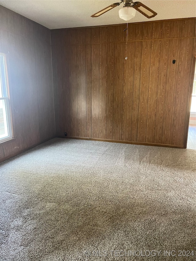 empty room featuring carpet, a textured ceiling, ceiling fan, and wooden walls