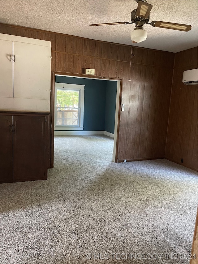 carpeted empty room featuring ceiling fan, wood walls, a textured ceiling, and a wall mounted AC