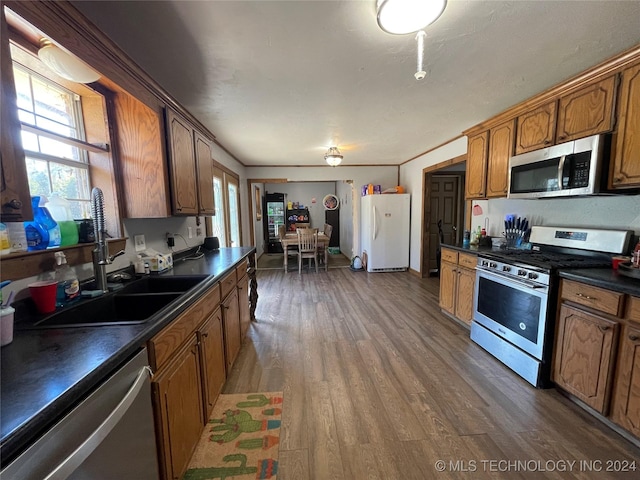 kitchen featuring brown cabinets, stainless steel appliances, dark countertops, a sink, and wood finished floors