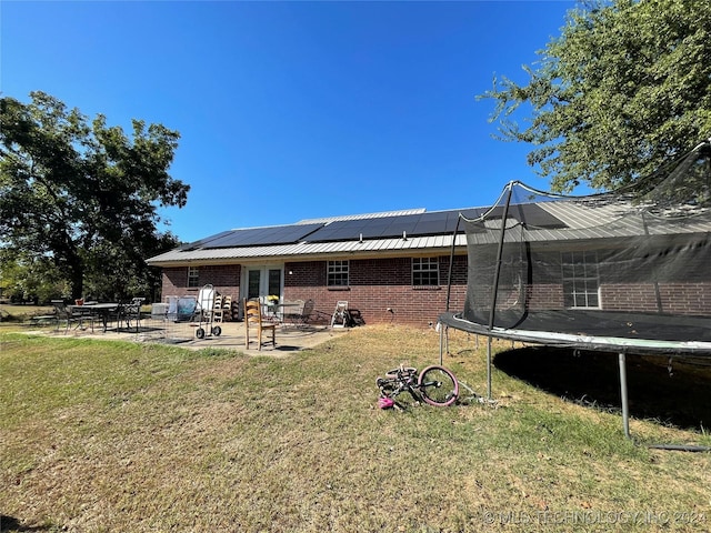 back of property with brick siding, a lawn, roof mounted solar panels, a trampoline, and a patio area