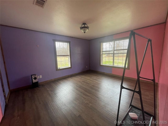 unfurnished room with a textured ceiling, dark wood-type flooring, visible vents, and baseboards