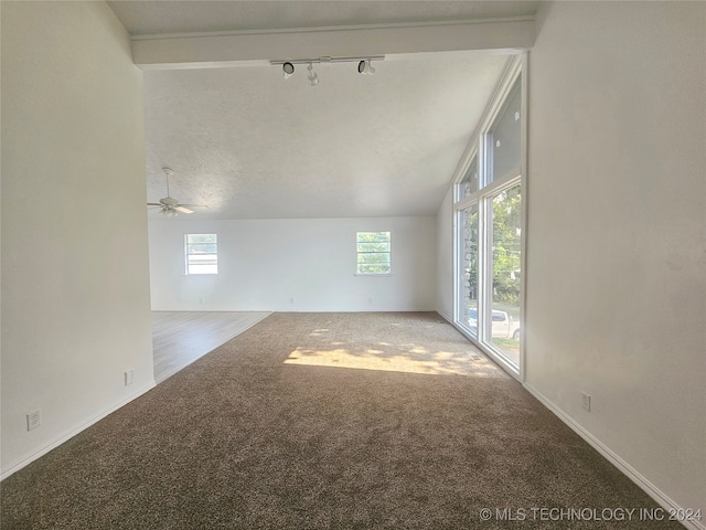 unfurnished living room featuring light colored carpet, lofted ceiling, rail lighting, ceiling fan, and a textured ceiling