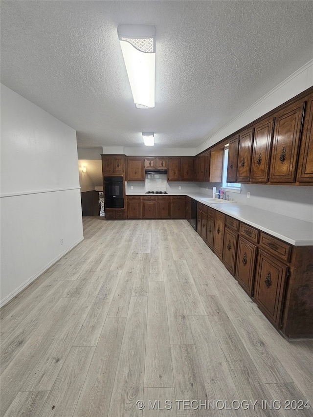 kitchen featuring sink, a textured ceiling, dark brown cabinetry, and light hardwood / wood-style flooring