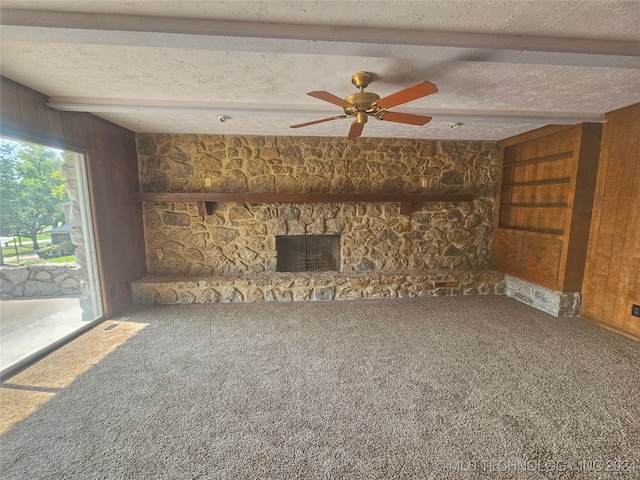 unfurnished living room featuring a textured ceiling, carpet flooring, ceiling fan, and a stone fireplace