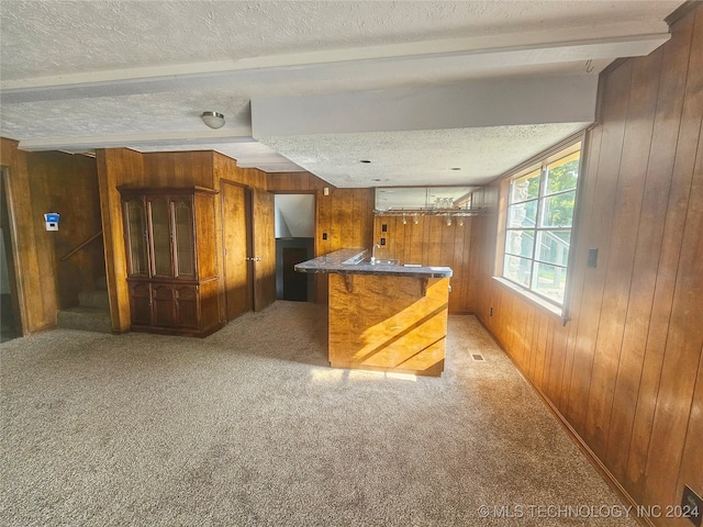 kitchen with wood walls, carpet flooring, beam ceiling, and a textured ceiling