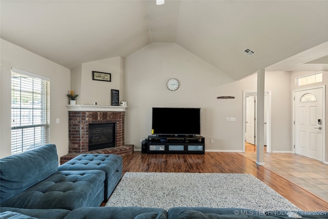 living room featuring lofted ceiling, wood-type flooring, decorative columns, and a brick fireplace