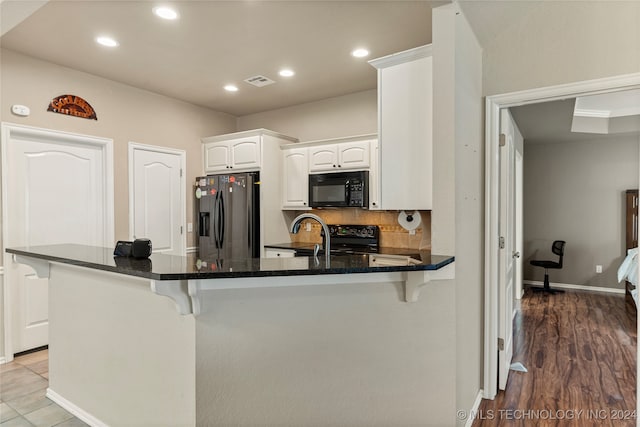 kitchen with black appliances, kitchen peninsula, a breakfast bar area, white cabinets, and light hardwood / wood-style floors