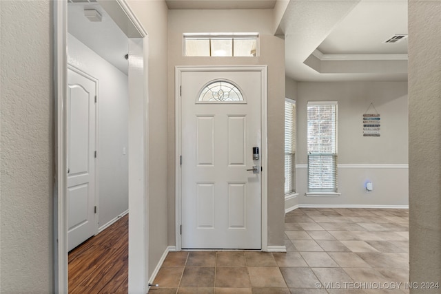 entryway with a healthy amount of sunlight, ornamental molding, a tray ceiling, and light hardwood / wood-style floors