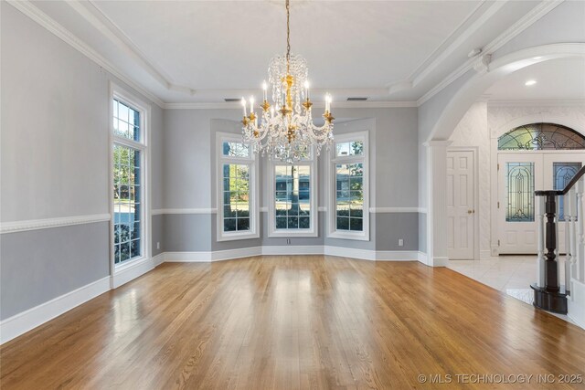 unfurnished dining area featuring ornamental molding, a raised ceiling, light hardwood / wood-style floors, and a notable chandelier