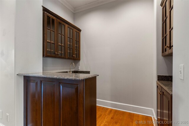 bar with crown molding, dark brown cabinetry, and dark stone counters