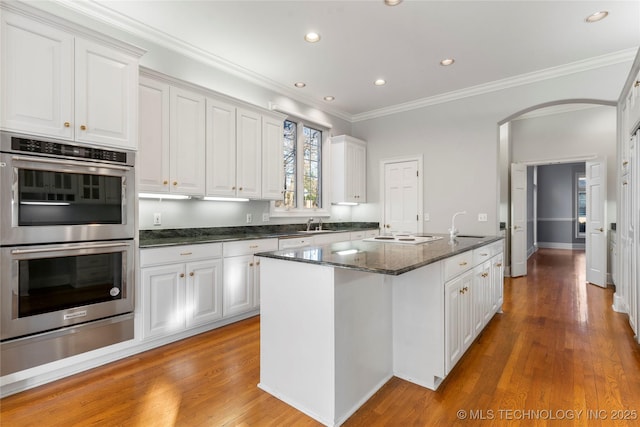 kitchen featuring white cabinetry, dark stone counters, an island with sink, and stainless steel double oven