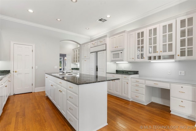 kitchen featuring sink, white cabinetry, built in appliances, dark stone countertops, and light hardwood / wood-style floors