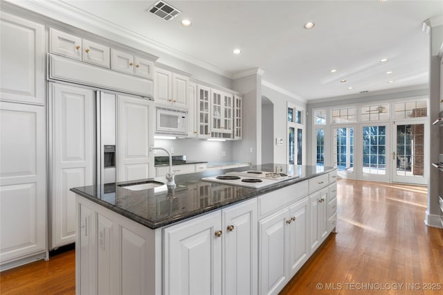 kitchen with built in appliances, sink, white cabinetry, and an island with sink