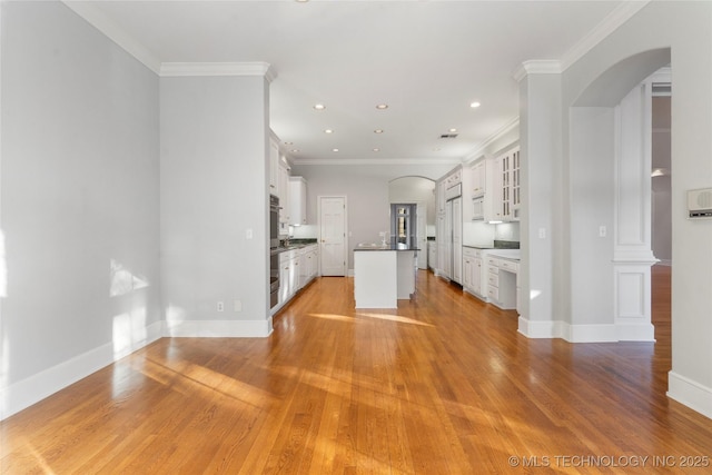 kitchen with white cabinetry, light hardwood / wood-style flooring, ornamental molding, and a center island with sink