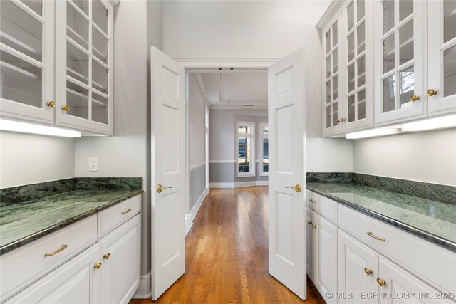 bar featuring dark stone countertops, light hardwood / wood-style floors, and white cabinets