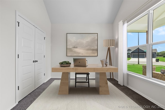 home office with lofted ceiling and dark colored carpet