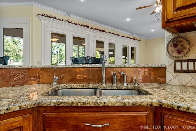 kitchen with ornamental molding, backsplash, light stone counters, sink, and ceiling fan