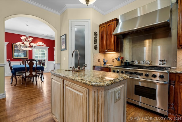 kitchen with an inviting chandelier, high end stove, sink, wall chimney range hood, and a center island with sink