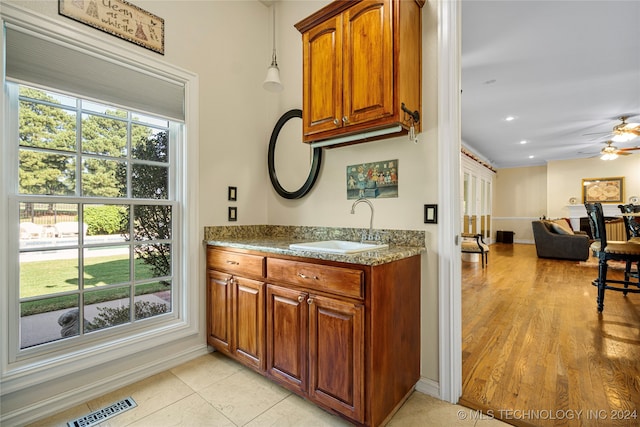 kitchen with dark stone countertops, light hardwood / wood-style flooring, sink, ceiling fan, and hanging light fixtures