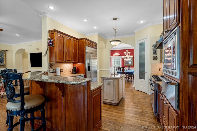 kitchen with light wood-type flooring, ornamental molding, built in appliances, kitchen peninsula, and light stone countertops