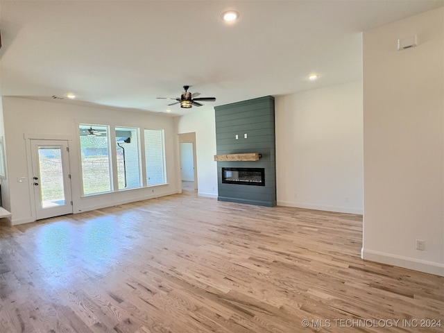 unfurnished living room with light wood-type flooring, a large fireplace, and ceiling fan