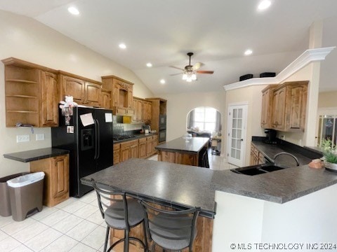 kitchen featuring a kitchen breakfast bar, kitchen peninsula, ceiling fan, black refrigerator with ice dispenser, and vaulted ceiling