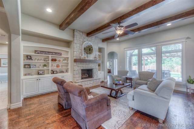 living room with dark hardwood / wood-style flooring, built in shelves, ceiling fan, beamed ceiling, and a stone fireplace