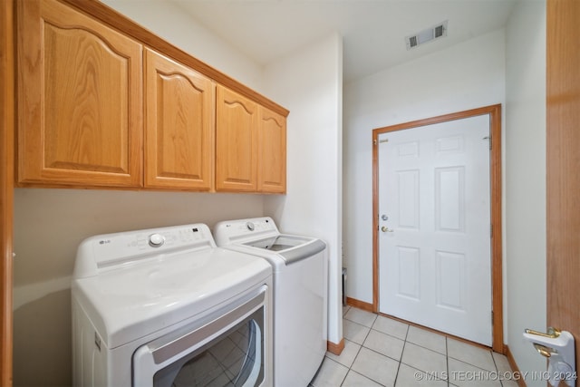 clothes washing area with cabinets, light tile patterned floors, and washing machine and clothes dryer