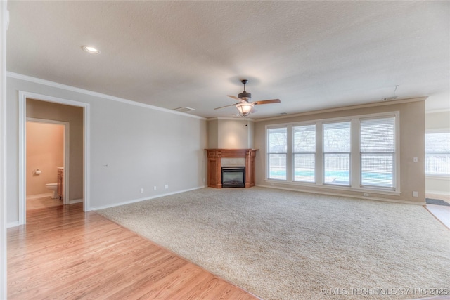 unfurnished living room with visible vents, crown molding, light wood-style floors, and a glass covered fireplace